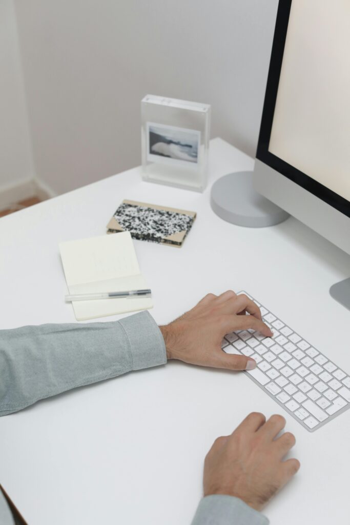 pexels photo 6177564 6177564 Crop faceless person using computer while working at table with notepad and pen in workplace